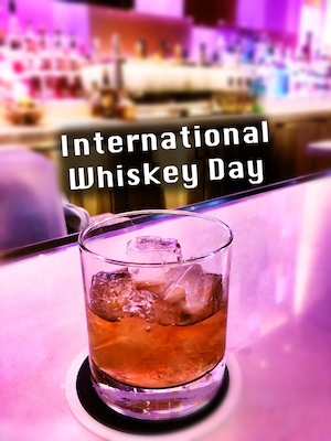 a short glass of whiskey on ice at a brightly colored bar for international whiskey day