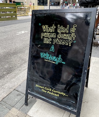 sidewalk sign outside a pizza shop used to promote a podcast