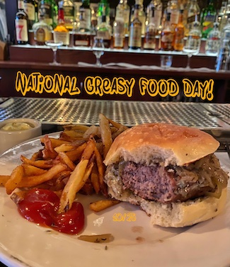 a medium cooked burger with onions and a huge bite taken out, with fries at a local bar for national greasy food day