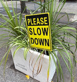 please slow down sign on busy city street
