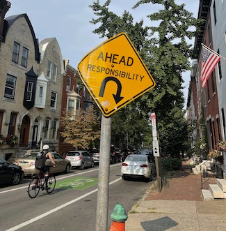 a city street with a bike rider in a bike lane and an American flag with a street sign that says ahead responsibility