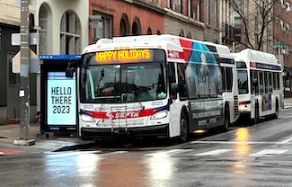 A bus stopped at a street corner on a city street showing happy holidays as its route
