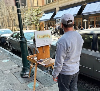 a street artist starting a new painting on a Sunday, on a city street, for an idea about the weekend from the daily thought blog www.caremoretoday.com