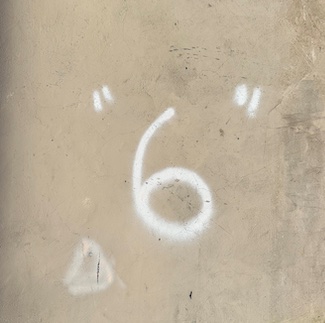 the number six spray painted in white on a tan concrete wall