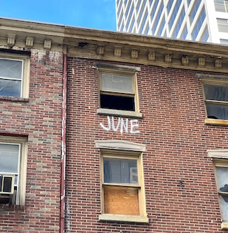 an abandoned brick building with an open window, and the word June spray painted on the wall below the window