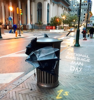 a city street garbage can filled with broken umbrellas 