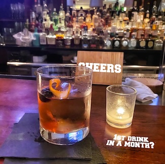 a whiskey drink on a wooden bar near a candle for a thought about dry January and the start of february