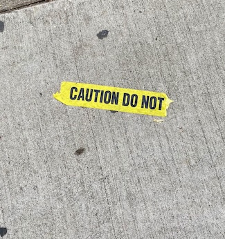 a small piece of torn caution tape on a cement sidewalk providing a warning thought for today
