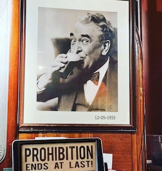 a photo of a man drinking a beer hanging on the wall in a bar to celebrate the end of prohibition in 1933