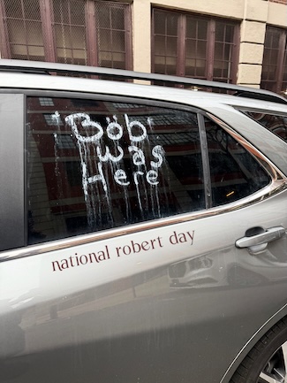 the words "Bob was here" hand written on the wide window of a silver car