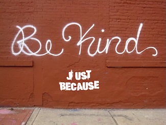 a painted red brick wall with the words "Be Kind", and "just because" spray paints on it
