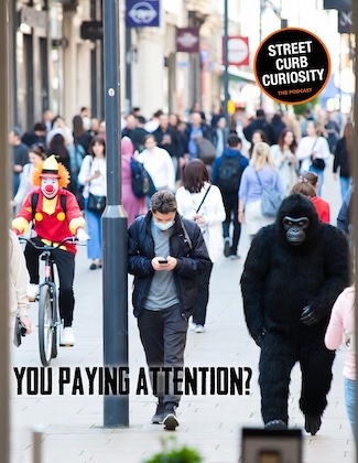 a young man walking on a busy street, oblivious to everything around him, including a guy in a gorilla suit and a clown.