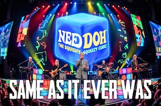 A rock band that looks like David Byrne and the Talking Heads on a bright colorful stage, performing with a huge blue cube called a Needoh behind the stage for a thought about boomers.