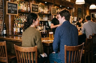 a young woman and guy sitting at a local bar with a beer and wine for national girlfriend day